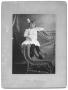 Photograph: [Unidentified girl in white dress on wicker chair]