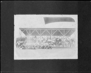 [A baseball team seated in front of covered grandstand area.]