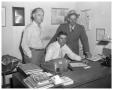 Photograph: Man in Pioneers shirt, with bat; men at desk