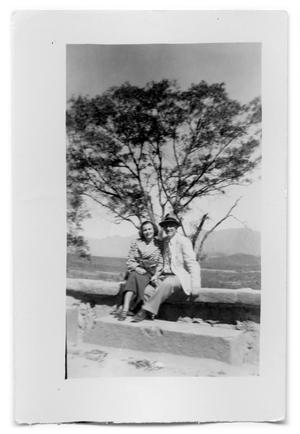 Vivian Osio and unknown man sitting on a stone wall
