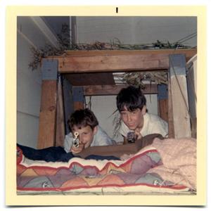 Two boys lying under a table with toy guns