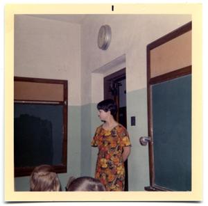 A gradeschool teacher standing next the entrance to a room