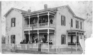 Two-story house with people gathered outside it.