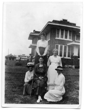 Five women posing together in the yard near a house