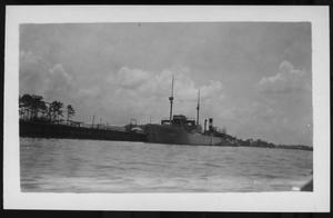 [Ship close to the bank of a river. Some buildings on the bank. Location unknown.]