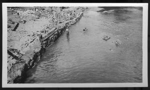 [Several people along the bank of a river, probably working. Location unknown.]