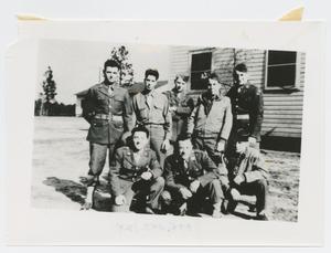 [Eight Soldiers Posing in Front of a Wooden Building]