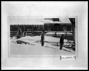 Two Men Pulling Sled in Front of Cabin