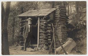 Primary view of object titled '[Postcard with Old Man Leaning on a Log Cabin]'.