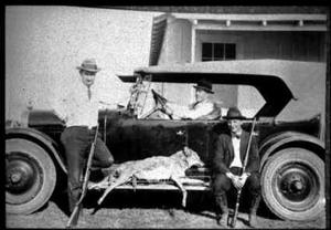 Primary view of object titled '[Three men around a car with a bagged coyote]'.