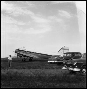 [Airplane in a Field with Three Cars and a Man]