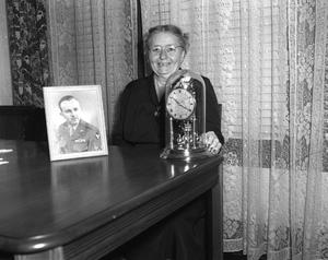 [Elderly Woman Posing with Clock and Portrait]