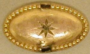 [Oval gold piece with a star engraved in the center]