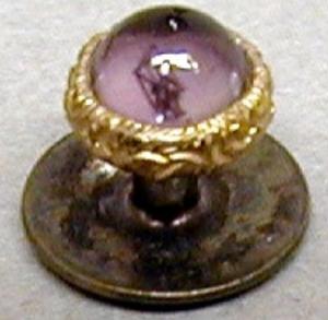 [One of a pair of gold cuff links with a purple stone attached on top]