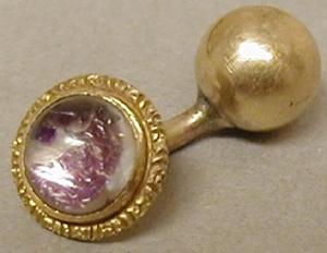 [One of a pair of gold cuff links with a purplish stone]