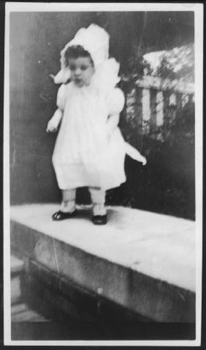 [Photograph of Mary Jones standing on a cement rail of the front porch leading to the George Ranch house]