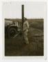 Photograph: [Man Standing by Pole and Vehicle]