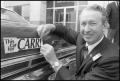 Photograph: [Photograph of Waggoner Carr Putting on a Bumper Sticker]