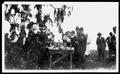 Primary view of [Group of men standing around a table drinking bottled beverages at Camp George]