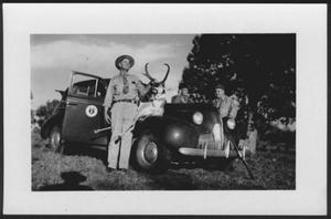 Primary view of [Three men standing around an automobile with a hunted deer on the hood]