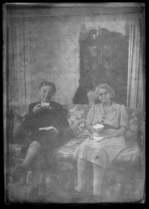 [Photograph of Mamie Davis George having a beverage on a sofa with an unidentified woman]