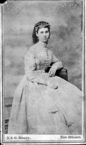 [A woman sitting on a chair, wearing a long, full dress]