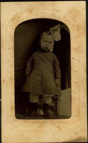 [A young boy standing and wearing a printed dress]