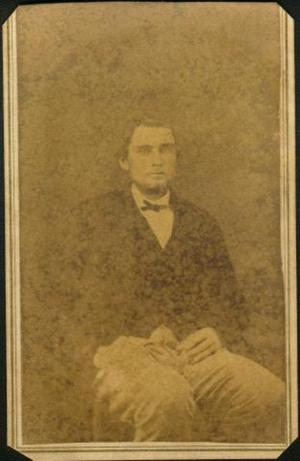 [A young man sitting in a chair with his right hand is in his pocket]