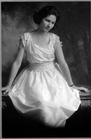 [An unidentified young woman sitting on a bench and wearing a white gown]