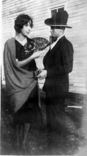 [A young woman and Len Martin standing in the yard, dressed up in dark clothing]