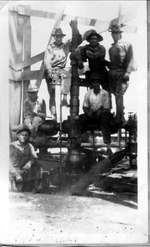Primary view of object titled '[Photograph of six men sitting on and around oil pipes]'.