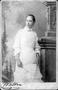 Photograph: [Woman wearing a white dress and standing by a large column]