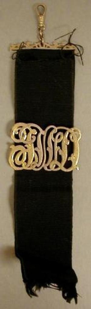 [Black ribbon watch fob with a gold clasp extending across the ribbon]