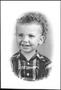 Photograph: [A child with short curly hair, wearing a plaid shirt and suspenders]