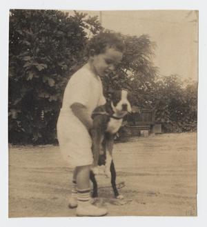 [Photograph of Child Standing While Holding a Dog]