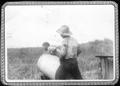 Photograph: [Two men lifting a steel drum in a field at the George Ranch]
