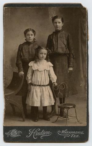 [Photograph of Three Girls Between Two Chairs]